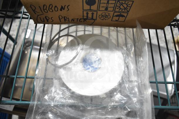 Box of 3 wax ribbons for UPS printer on metal shelf. Box marked with handling symbols. Items in plastic wrap.