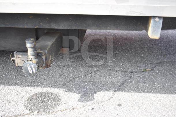 Close-up of a 2021 Texino food trailer hitch. Triple-axle design, in good condition. Road surface visible beneath.