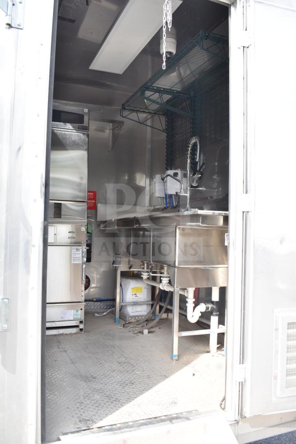 Interior of a 2021 Texino 28ft food trailer featuring a stainless steel sink, shelving, and commercial kitchen equipment.