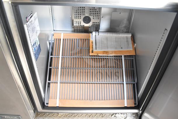 Interior view of Texino 2021 food trailer's True refrigeration unit, showcasing steel shelves and product documentation.