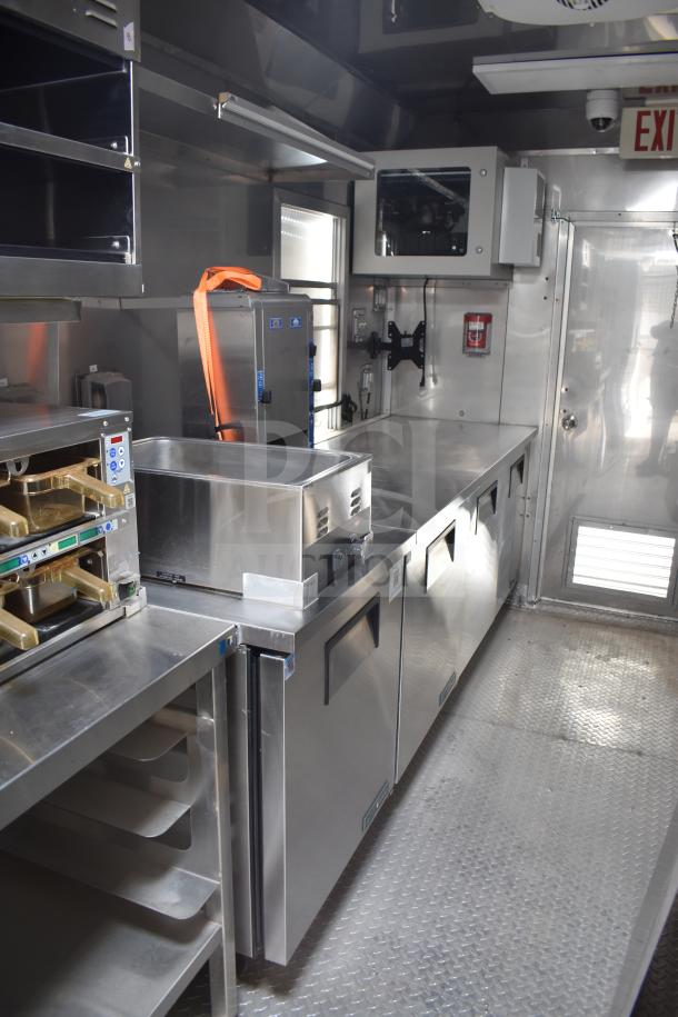 Interior of a new 2021 Texino 28ft triple-axle food trailer with stainless steel appliances, CaptiveAire hood, Ultrafryer 4-bay fryer, True refrigeration, and Winston CVap holding unit.