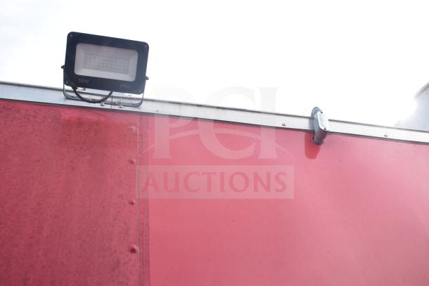 Red exterior of 2021 Rock Solid Cargo 28ft food trailer. Visible 50W IP66 floodlights, triple-axle design.