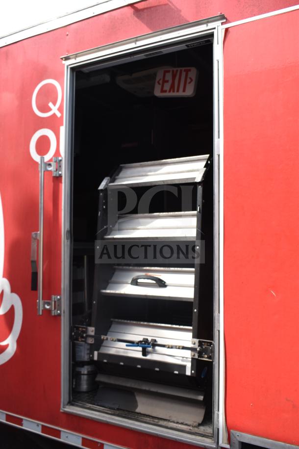 2021 Rock Solid Cargo 28ft food trailer, open side door revealing interior. Visible exit sign inside. Exterior red with graphics.