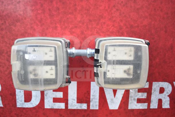 Electrical outlets with protective covers, labeled for wet locations, mounted on a red surface displaying partial "DELIVERY" text.