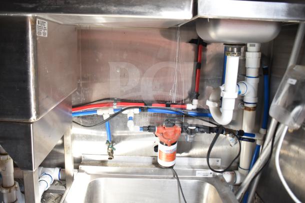 Interior plumbing of a 2021 Rock Solid Cargo 28ft triple-axle food trailer, showcasing pipes and fittings beneath the sink.