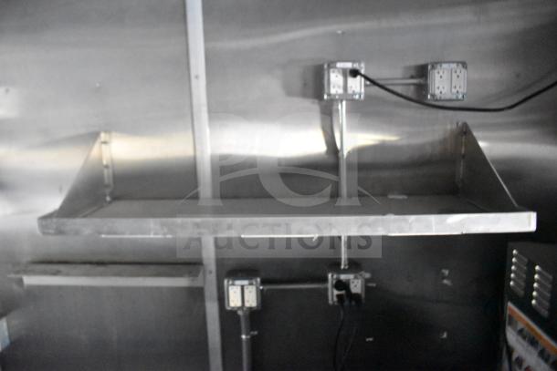 Interior view of a 2021 Rock Solid Cargo 28ft food trailer with metal shelf and electrical outlets, showcasing part of its kitchen setup.