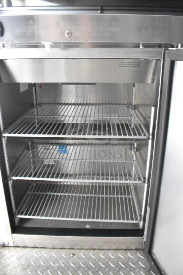 Interior view of a commercial food trailer refrigerator. Features three wire shelves, stainless steel finish, and industrial-grade construction.