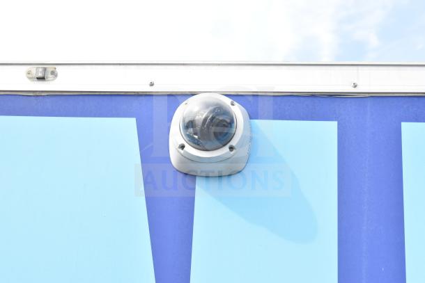 A white security camera mounted on the exterior of a blue food trailer.