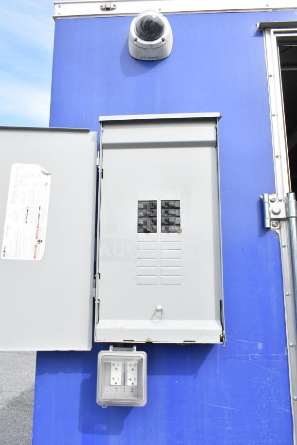 Electrical panel on the NBRHD Kitchens Ghost Kitchen Food Trailer, featuring circuit breakers and a mounted CCTV camera.