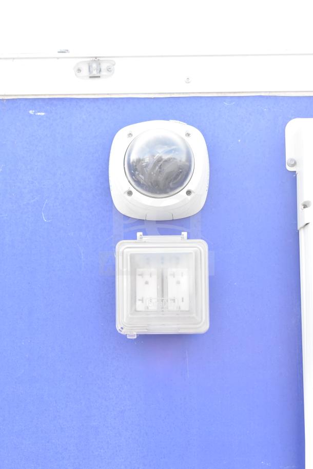 Food trailer with security camera and weatherproof electrical outlet on a blue exterior.