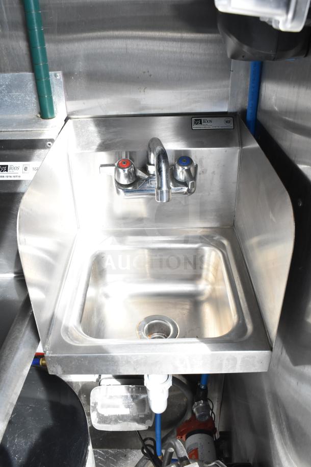 Stainless steel sink in NBRHD Kitchens food trailer, featuring dual faucets, branded by John Boos, with visible plumbing and labels.