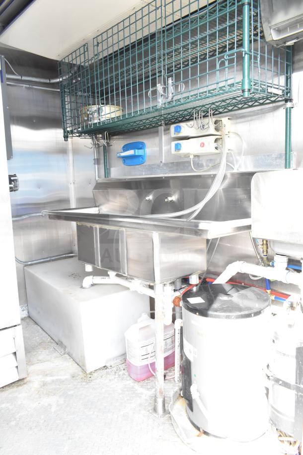 NBRHD Kitchens food trailer interior with stainless steel sink, shelving, visible piping, and utility connections.