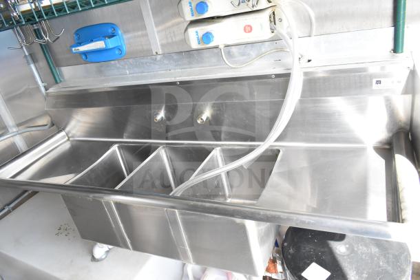 Stainless steel sink with triple basins in a food trailer. Features include Ecolab dispensers and modern plumbing fittings.