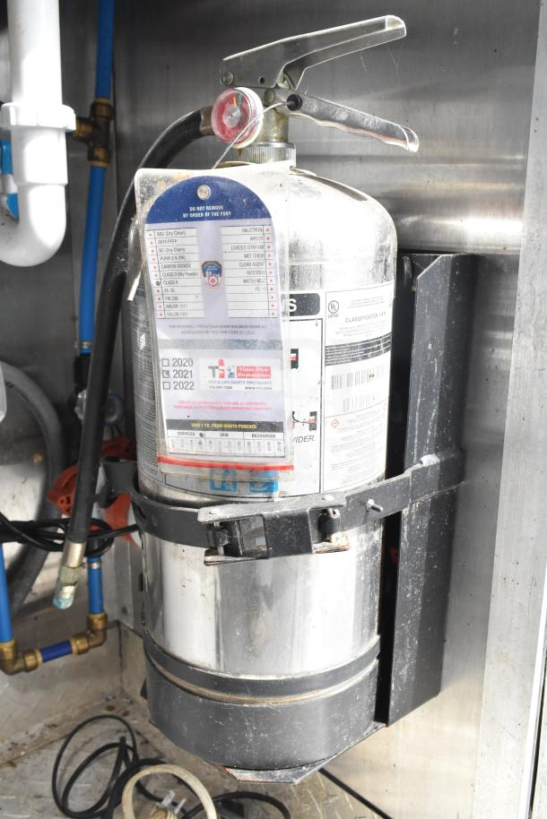 Fire extinguisher mounted in NBRHD Kitchens food trailer, visible inspection tags for 2020-2022.