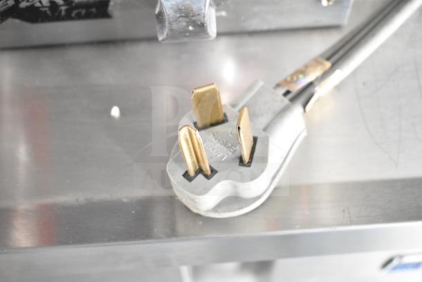 Electrical plug detail on NBRHD Kitchens food trailer. Shows plug type and condition, featuring metal prongs on stainless steel surface.