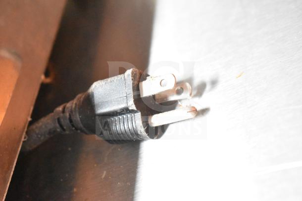 A close-up of a three-pronged electrical plug, showing signs of wear and mild discoloration on the prongs.