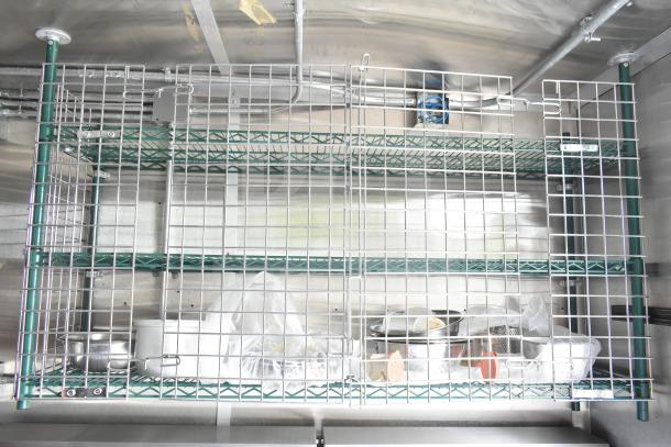 NBRHD Kitchens Ghost Kitchen trailer interior featuring wire shelving with storage bins and kitchen supplies.