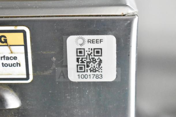 QR code label on metal surface, marked "REEF" with code "1001783" visible. Nearby warning label indicates caution for hot surfaces.