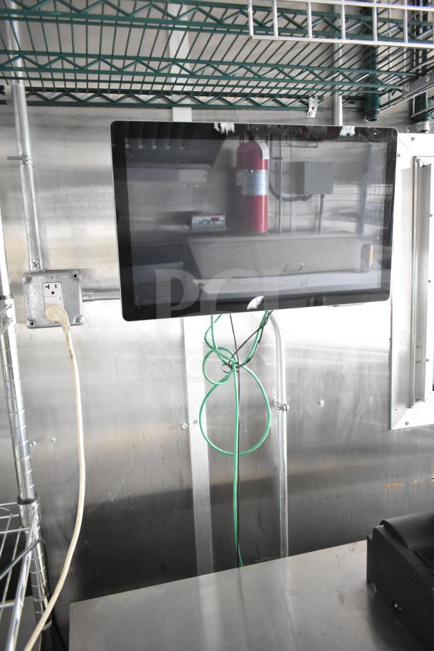 Food trailer interior with mounted monitor, power outlet, and stainless steel surfaces. Shelving and cables visible.