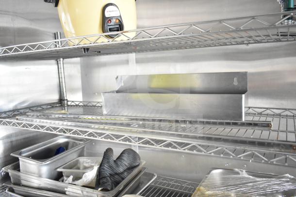 NBRHD Kitchens food trailer interior; metal shelving with trays, gloves, and a Hamilton Beach appliance.
