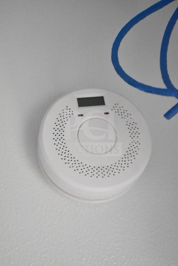 Close-up of a white ceiling-mounted device with digital display and vent holes, next to a blue cable.