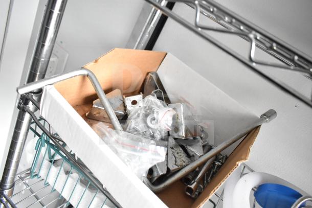 Box of metal brackets, screws, and fittings on a wire shelf inside the 2020 Southern Dimensions trailer.