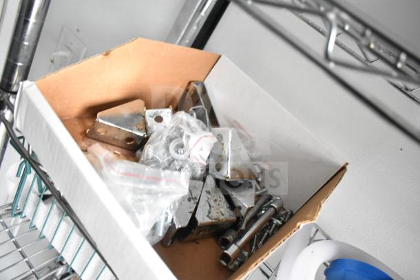 Box of assorted metal brackets and hardware on wire shelving, part of trailer contents.