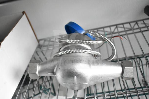 Metal component with wiring and blue cap, resting on wire shelving. Appears unused, suitable for industrial or technical use.