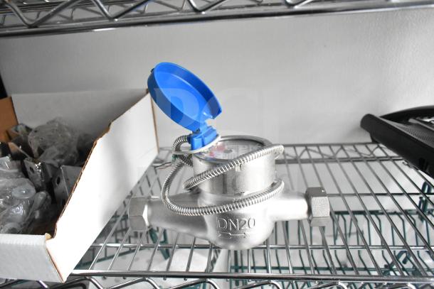A DN20 water flow meter with a blue lid on a wire shelf, surrounded by packaging materials.