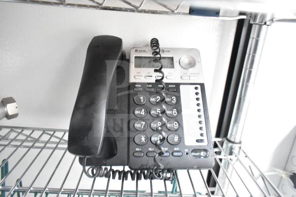 A black office phone with push-button keypad sits on a wire shelf, part of a mobile commissary trailer's interior.