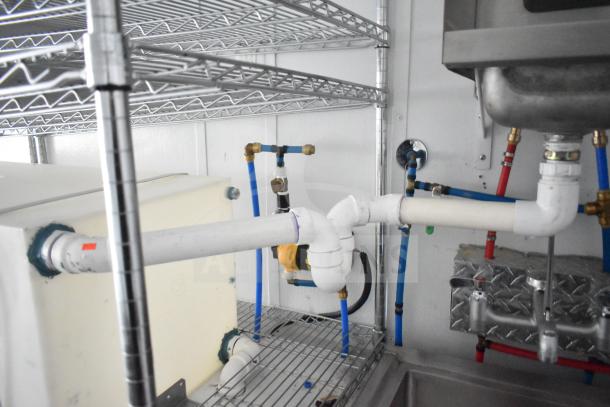 Interior plumbing and shelving of a 2020 Southern Dimensions Group mobile commissary trailer. Visible piping and wire shelves.