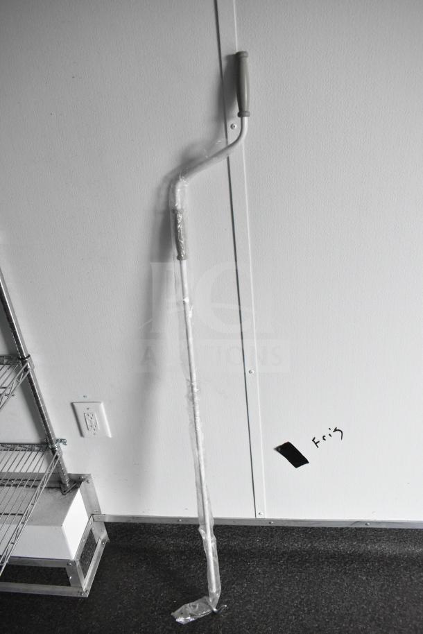 A long handle tool leaning against a white wall next to metal shelving.