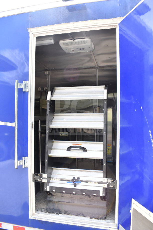 Blue 2021 Rock Solid Cargo 28ft food trailer with open side door showing interior shelves. Includes refrigeration and Nieco Charbroiler.