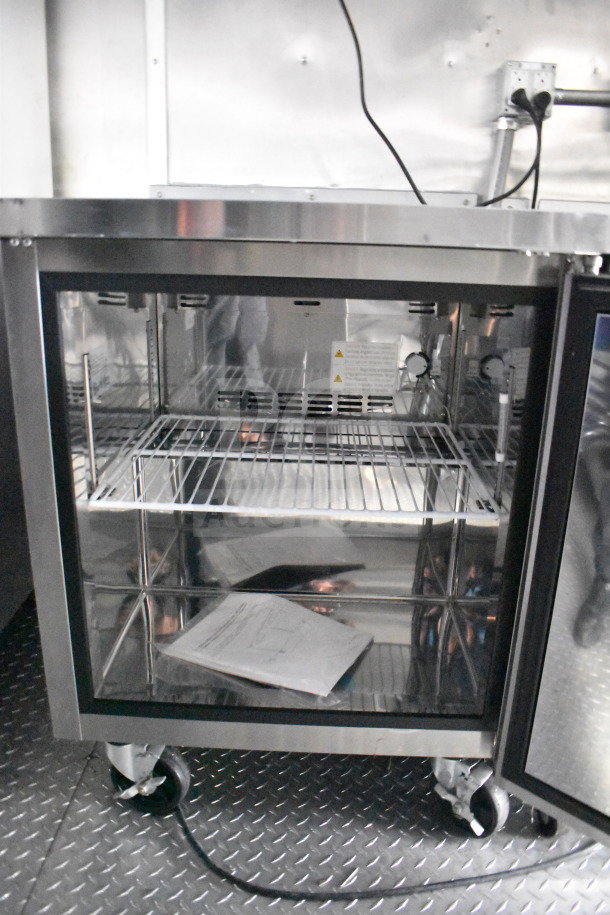 Stainless steel refrigerator in a 2021 Rock Solid Cargo food trailer; features glass door, shelves, and mobile casters.