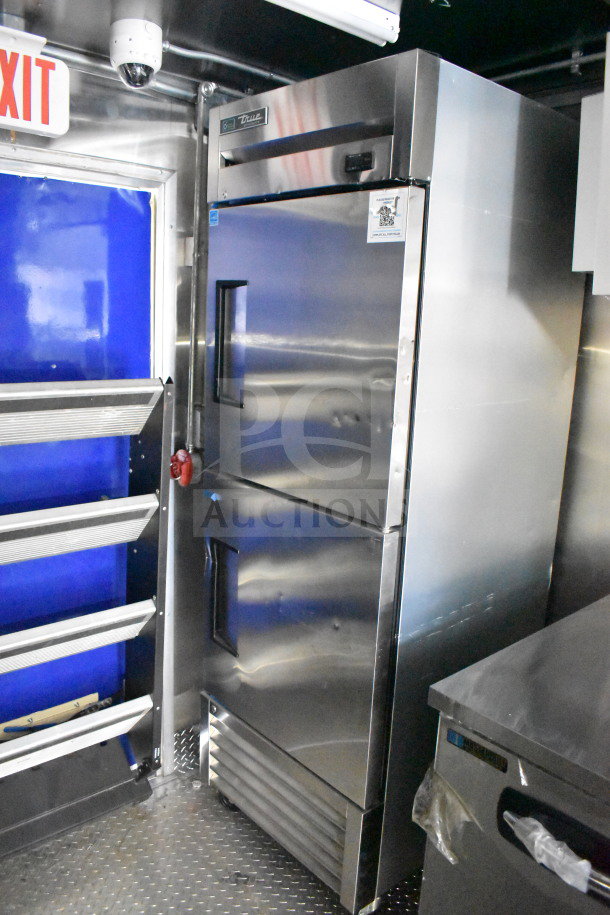 New 2021 Rock Solid Cargo 28ft food trailer interior, featuring a stainless steel True refrigerator, CaptiveAire hood, and shelving.