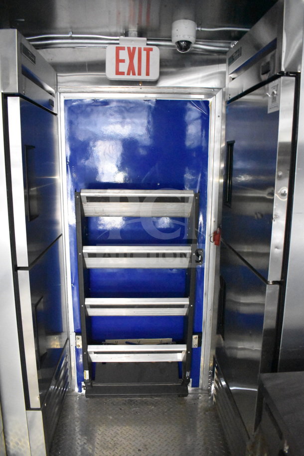 Interior of a 2021 Rock Solid Cargo 28ft food trailer showing commercial refrigeration units, a blue wall, and an exit sign.