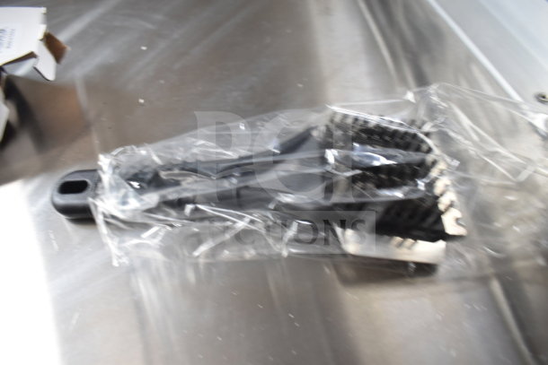 Plastic-wrapped grill brush on a steel surface, part of the Rock Solid Cargo 28ft food trailer equipment package.
