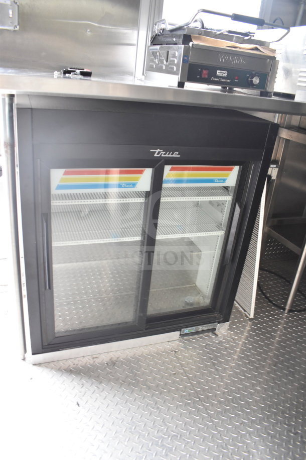 True sliding glass door refrigerator inside 2021 Rock Solid Cargo food trailer. New condition, stainless steel finish.
