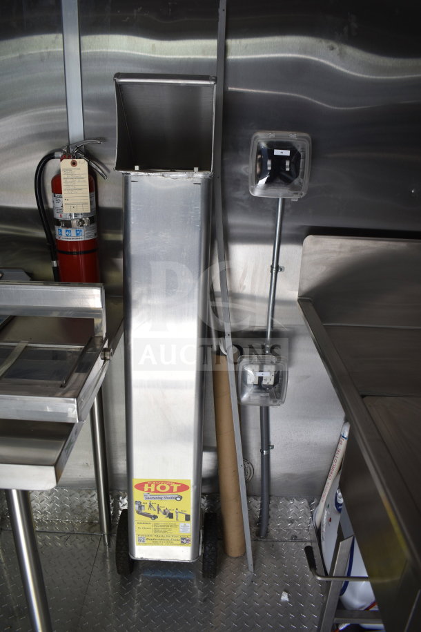 Interior view of a new 2021 Rock Solid Cargo 28ft commercial food trailer, featuring stainless steel surfaces, a fire extinguisher with inspection tag, and electrical outlets.