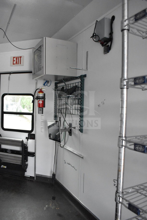 All-black mobile commissary/command trailer interior with IT/network cabinet, wire shelving, and Coleman Mach AC.