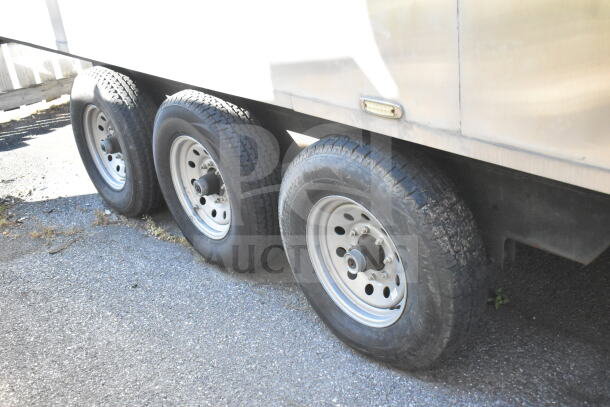 Triple-axle wheels of 2021 Texino 28ft cooking trailer, street view. Sturdy tires, metallic rims visible.