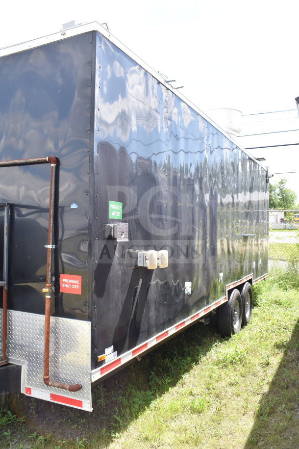 2021 Cruising Kitchens 8.5'x24' food trailer, black exterior, dual axles, labeled for potable water and propane shut off.