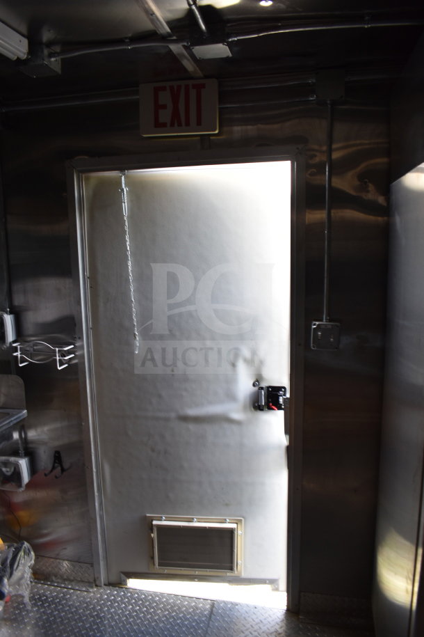 Interior view of 2021 Cruising Kitchens 8.5'x24' food trailer, featuring an exit door, wall shelving, and stainless steel surfaces.