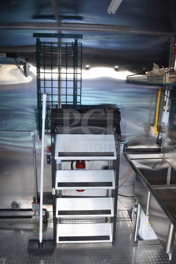 Interior of 2021 Cruising Kitchens 8.5'x24' food trailer, featuring a metal shelf, mop, fire extinguisher, and stainless steel sink.