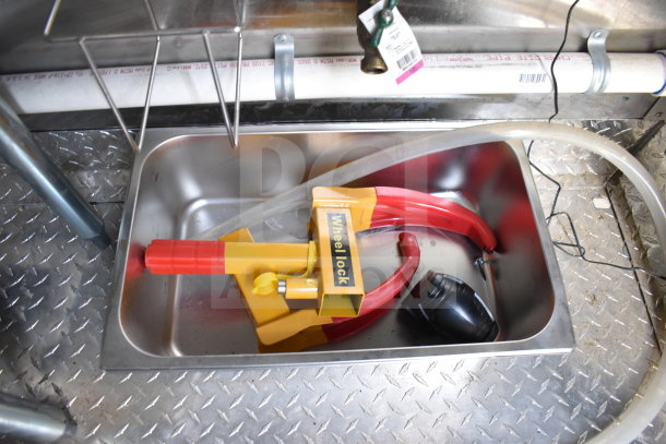 Wheel lock in metal tray on diamond plate floor of 2021 Cruising Kitchens food trailer. Includes pipe and tag above.