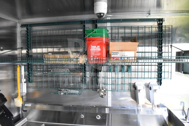 2021 Cruising Kitchens food trailer interior with metal shelving, a grease hood, cleaning supplies, and a camera.