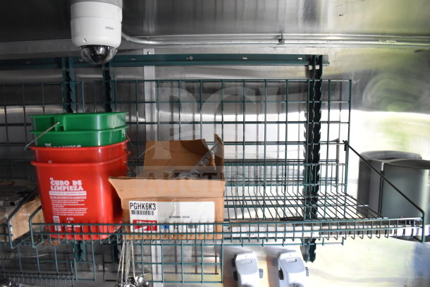 Inside view of the 2021 Cruising Kitchens 8.5'x24' food trailer, featuring shelving with red and green cleaning buckets and a cardboard box.