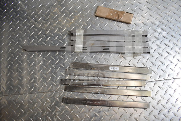 Metal strips and a wrapped package on diamond plate flooring. Metal strips have barcode labels and visible distress marks.