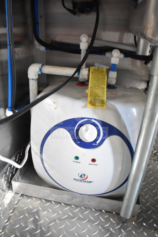 Inside view of the 2021 Cruising Kitchens 8.5'x24' food trailer, showing plumbing components and an Eccotemp unit on a diamond plate floor.