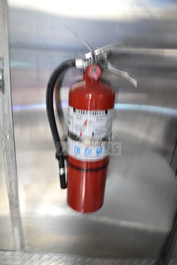 Red fire extinguisher mounted on a metallic wall inside a 2021 Cruising Kitchens food trailer, part of safety equipment.